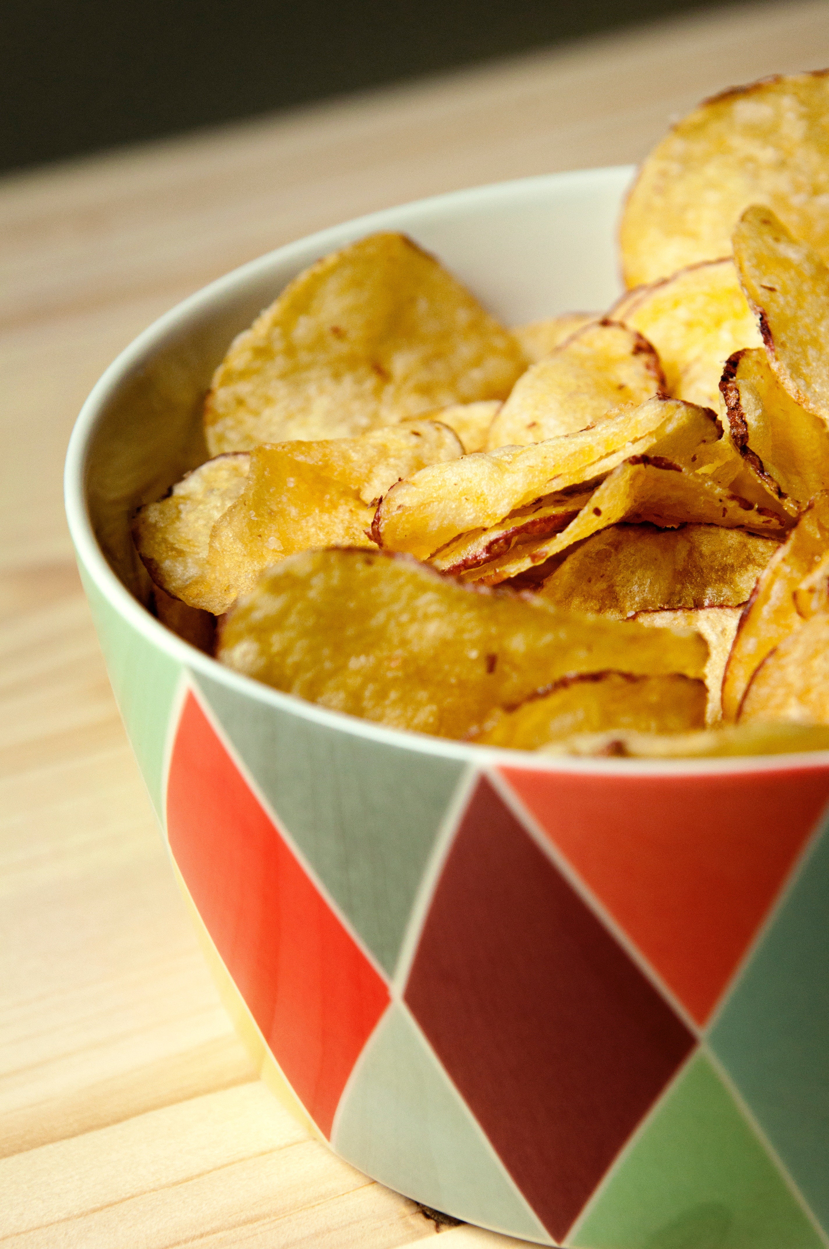 Batatas chips douradas numa tigela de cerâmica colorida sobre a mesa de madeira.